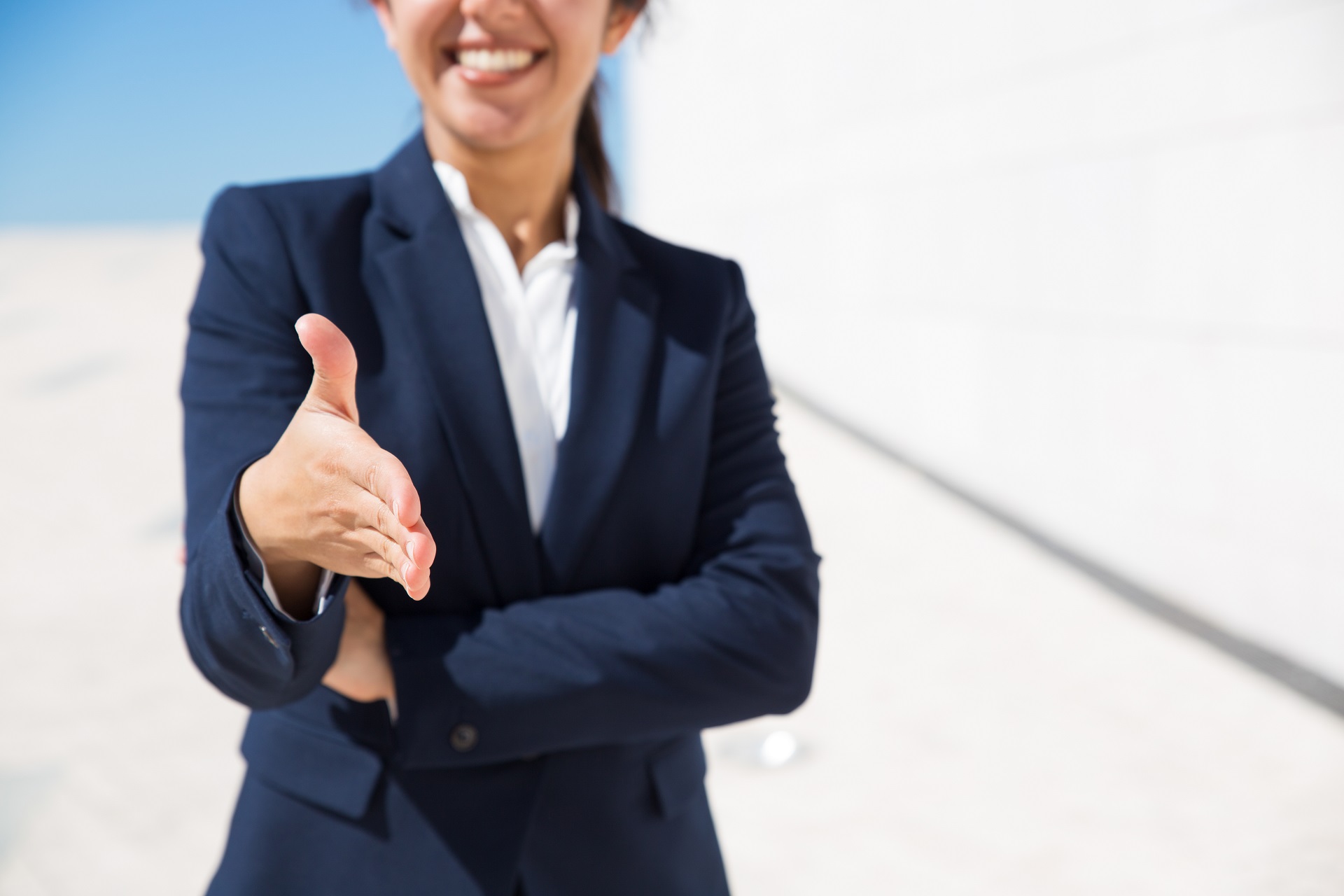 Smiling HR manager congratulating with getting job. Cropped portrait of positive woman in formal suit standing outdoors and offering hand for handshake. Business offer concept